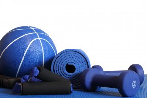 A yoga mat, a medicine ball, two 3lb dumbbells, and medium-resistance stretch tubing rest on a workout mat. The white background offers opportunity for clipping or the placement of text and/or graphics.